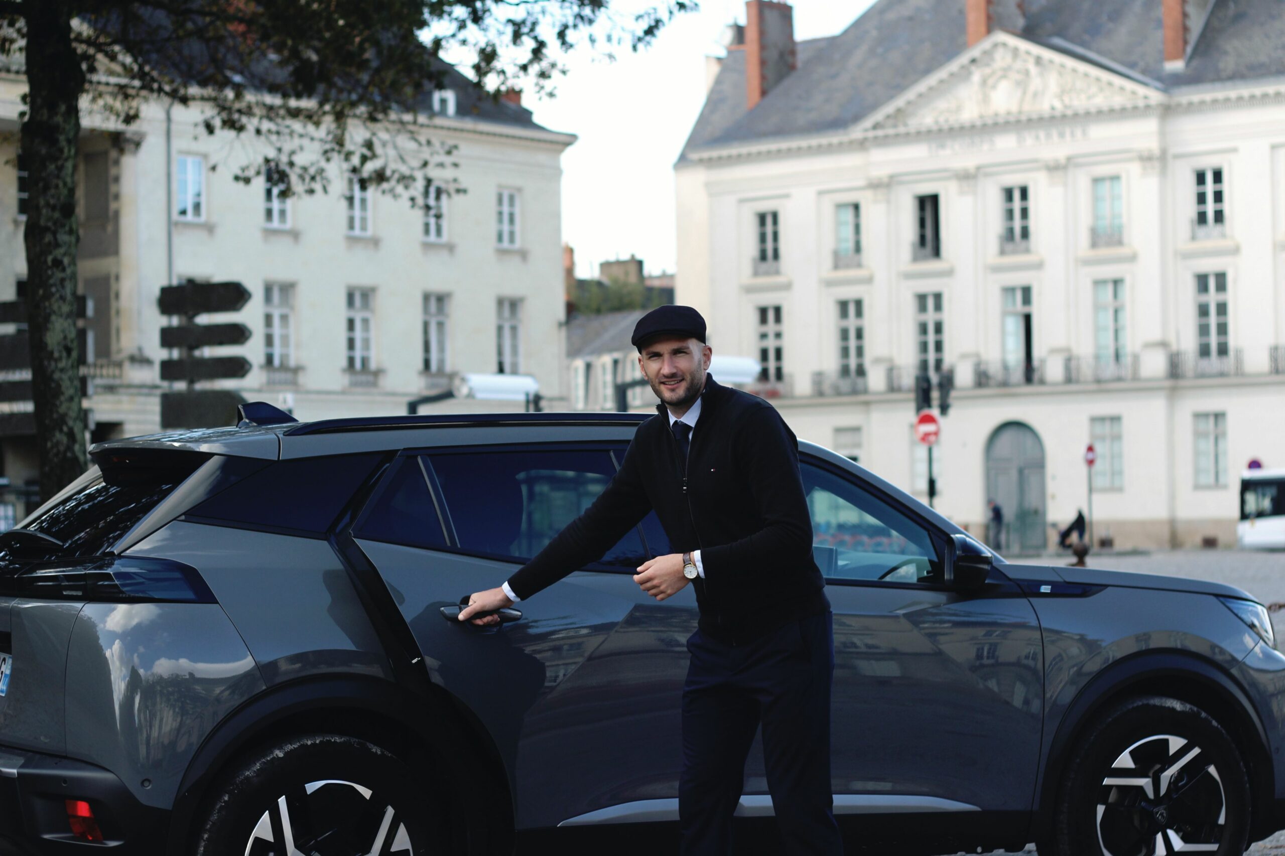 Un chauffeur élégant et avenant s'empresse d'ouvrir la portière d'un peugeot e2008 gris foncé parfaitement propre devant l'Hôtel d'Aux, ancien siège du XIe corps d'armée longeant le cours Saint-André et donnant sur la place du Maréchal-Foch à Nantes.