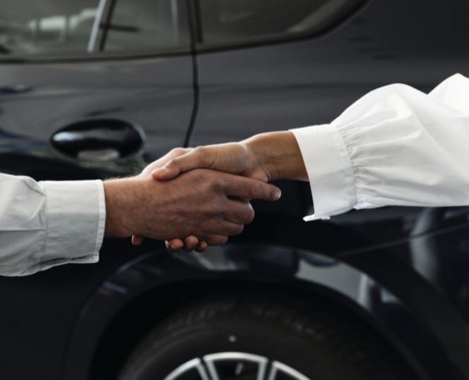 Une poignée de main professionnelle en premier plan devant une berline noire en arrière plan. Deux personnes fiables se poignent la mains